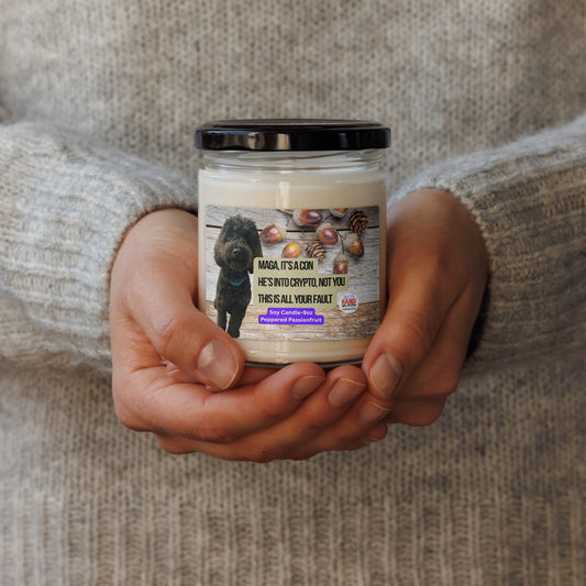 Person in a beige sweater holds a candle in a glass jar with lid. The label shows a black dog superimposed on a horizontal wood plank background with acorns scattered top right. In the center, the political, satirical, anti-MAGA haiku in black text with tan background is shown. It reads:
MAGA It's a Con
He's Into Crypto, Not You
This is All Your Fault
Bottom center is white text on a purple background that reads Soy Candle - 9oz Peppered Passionfruit.
The text logo for leoshaiku.com is bottom right.