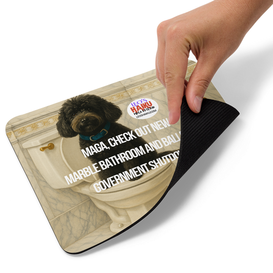 A hand holds up the right bottom edge of standard mouse pad printed with the image of a small black dog sitting on top of a toilet seat. Bathroom is very ornate, marble and gold, with a tall gold toilet paper holder. Political, satirical, anti-mage haiku is displayed as is the text logo of leoshaiku.com This view shows the thickness of the pad.