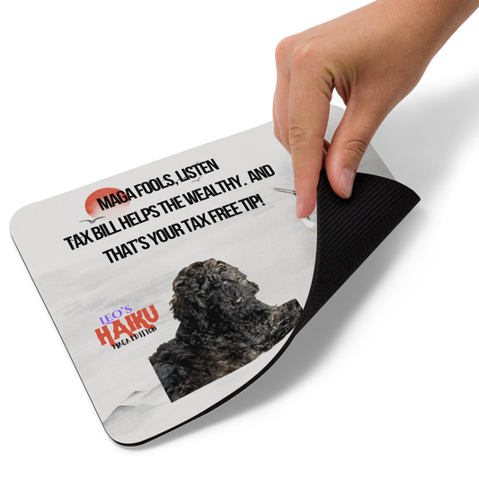 A hand lift the bottom right corner of a standard-sized mouse pad printed with a light background with an oriental theme including a red sun, a heron and distant mountains. A poodle and political satire in Haiku format are super-imposed on the design. This view shows the thickness of the pad.