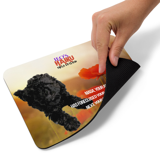 Hand lifts the bottom right corner of standard-sized mouse pad printed with a background of red poppies and other plants, a reclining dog, and political satire in Haiku format.