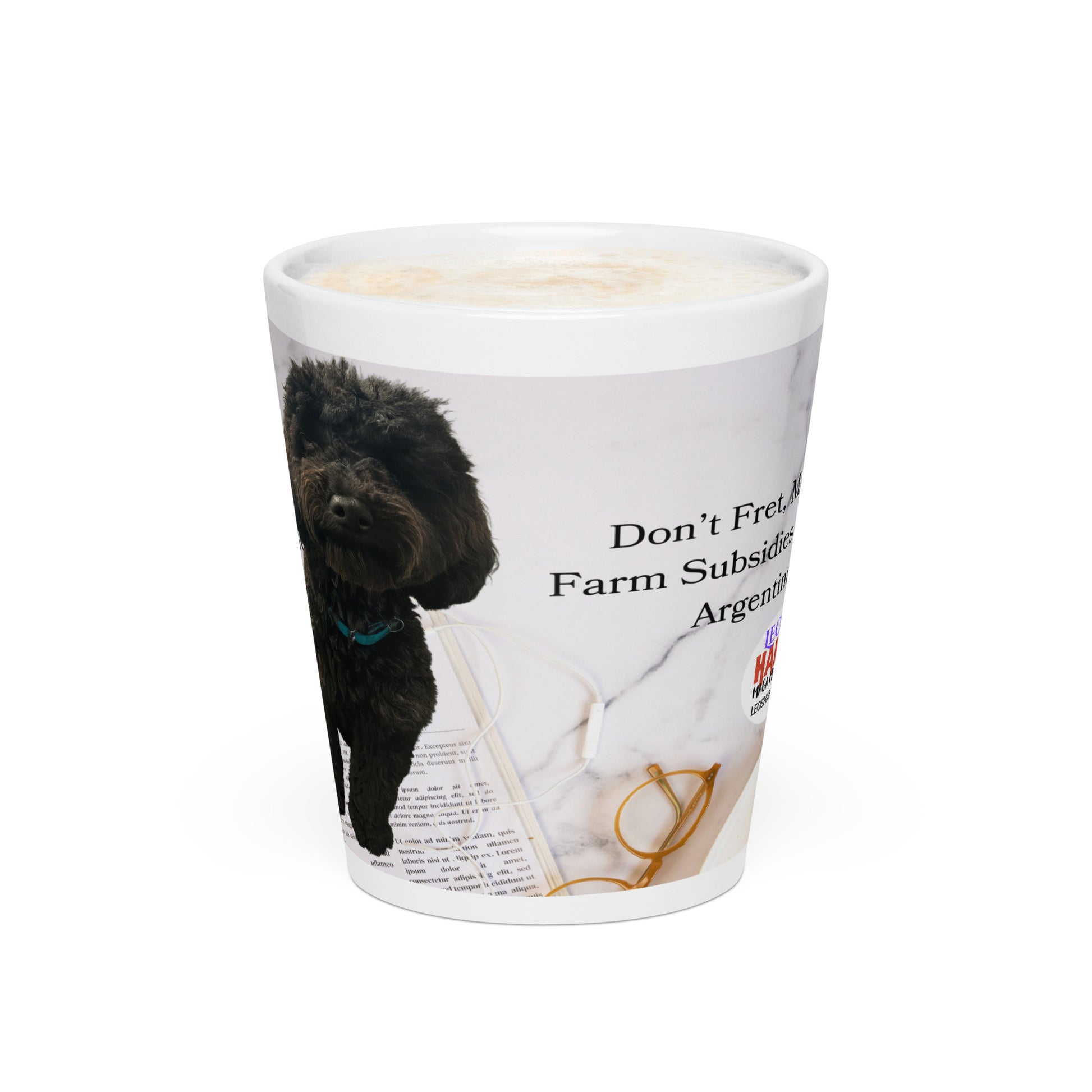 White glossy ceramic mug printed with image of a kitchen counter with a back dog sitting on a newspaper and glasses.  Political, satirical, anti-MAGA haiku is partially visible as is the text logo for leoshaiku.com