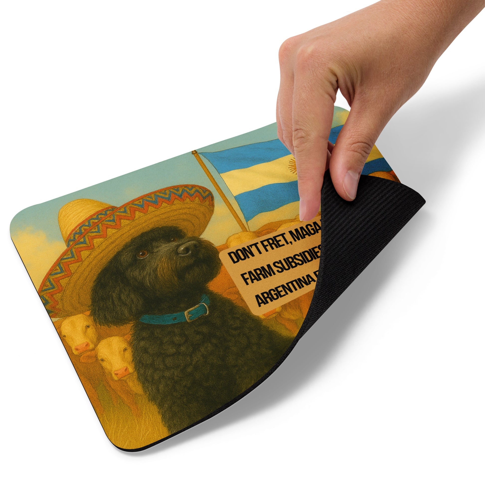 A hand lifts the bottom right corner of a Standard Mouse Pad printed with the image of small black dog with a sombrero.  He sits in front of a herd of cows.  The Argentina flag flies above them to the right of the dog.  Under the flag is a political, satirical, anti-MAGA haiku that reads:
Don't Fret, MAGA Fools.
Farm Subsidies Coming. BUT, ARGENTINA FIRST!
The circular text logo for leoshaiku.com is centered beneath the haiku.
This view shows the thickness of the pad.