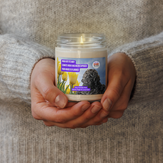 A person in a wheat-colored wool sweater holds a lighted candle in a glass jar.  The candle has a label that shows the image of a black dog lying near a group of yellow tulips. Top left is a political, satirical, anti-MAGA haiku, white text on a purple background, reads:  
MAGA got its way
Climate Hoax has been exposed
Your house is flooded.
Top right is the text logo for leoshaiku.com; Bottom center is another text bubble that reads Soy Candle 9 oz; White Sage and Lavender