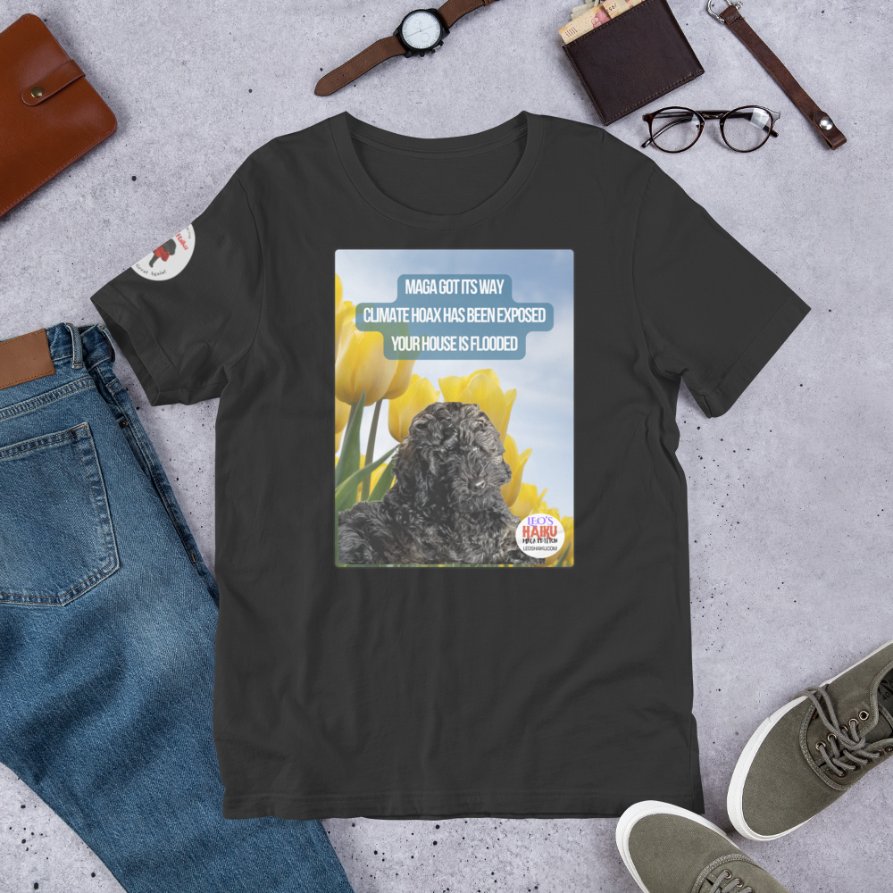 Dark gray t-shirt with a graphic design featuring text and an image of Leo the mini poodle.  Shirt is on a gray surface with jeans, shoes, and accessories.  Design on the shirt is Leo in a field of tulips under a blue sky.  A political, satirical, anti-MAGA haiku reads:
MAGA Got Its Way
Climate Hoax Has Been Exposed
Your House Is Flooded
The circular text logo for leoshaiku.com is bottom right.