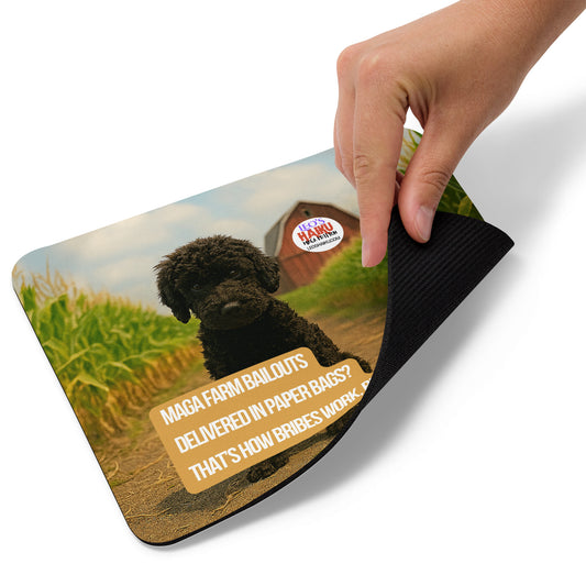 Standard sized mouse pad with a hand lifting the lower right corner.  Leo the black mini poodle sits in a cornfield.  In the distance a red barn has the text logo for leoshaiku.com.  In the foreground, a political, satirical, anti-MAGA haiku says:  
MAGA Farm Bailouts
Delivered in Paper Bags?
That's How Bribes Work, Right?
This view shows the thickness of the pad.
