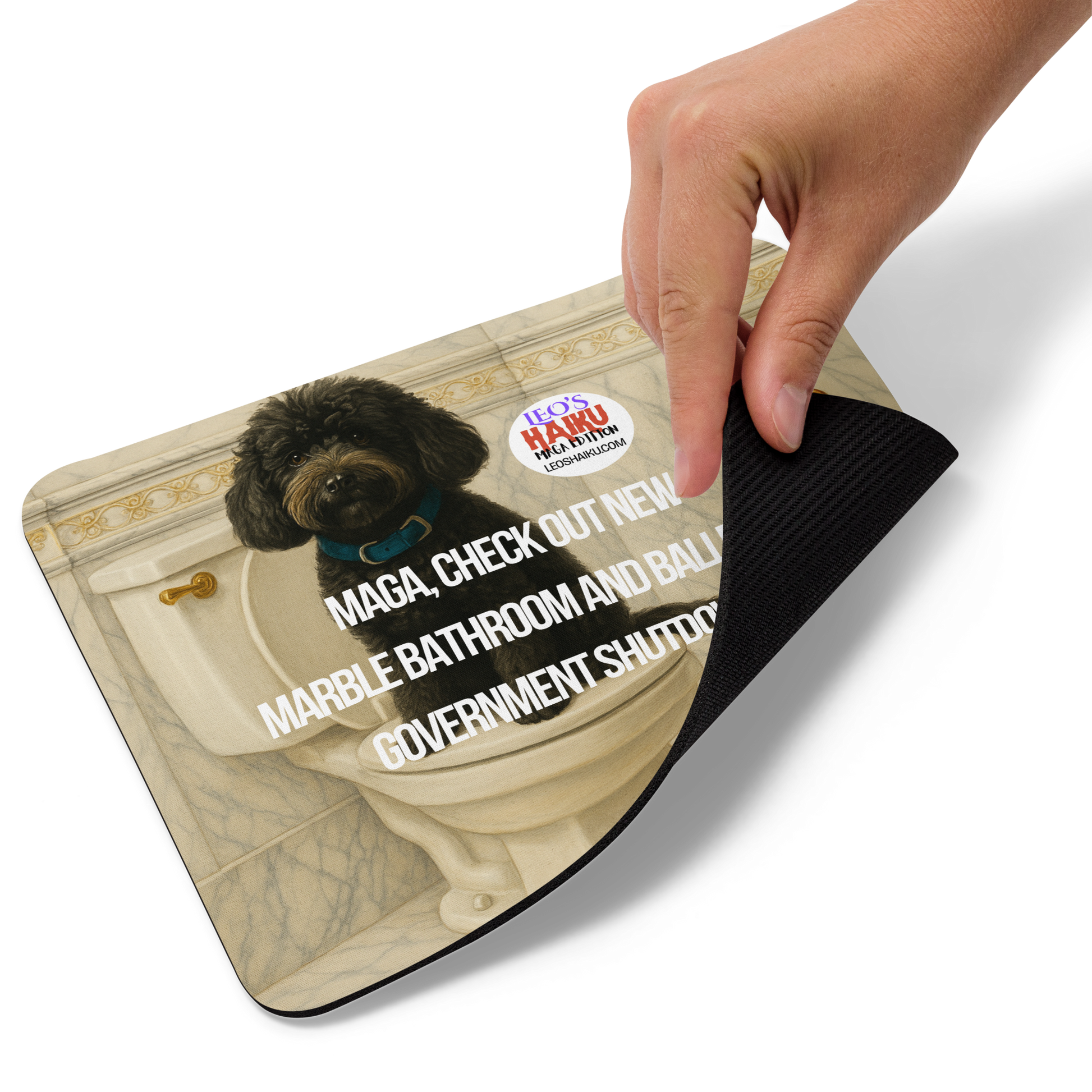 A hand holds up the right bottom edge of standard mouse pad printed with the image of a small black dog sitting on top of a toilet seat.  Bathroom is very ornate, marble and gold, with a tall gold toilet paper holder.  Political, satirical, anti-mage haiku is displayed as is the text logo of leoshaiku.com  This view shows the thickness of the pad.