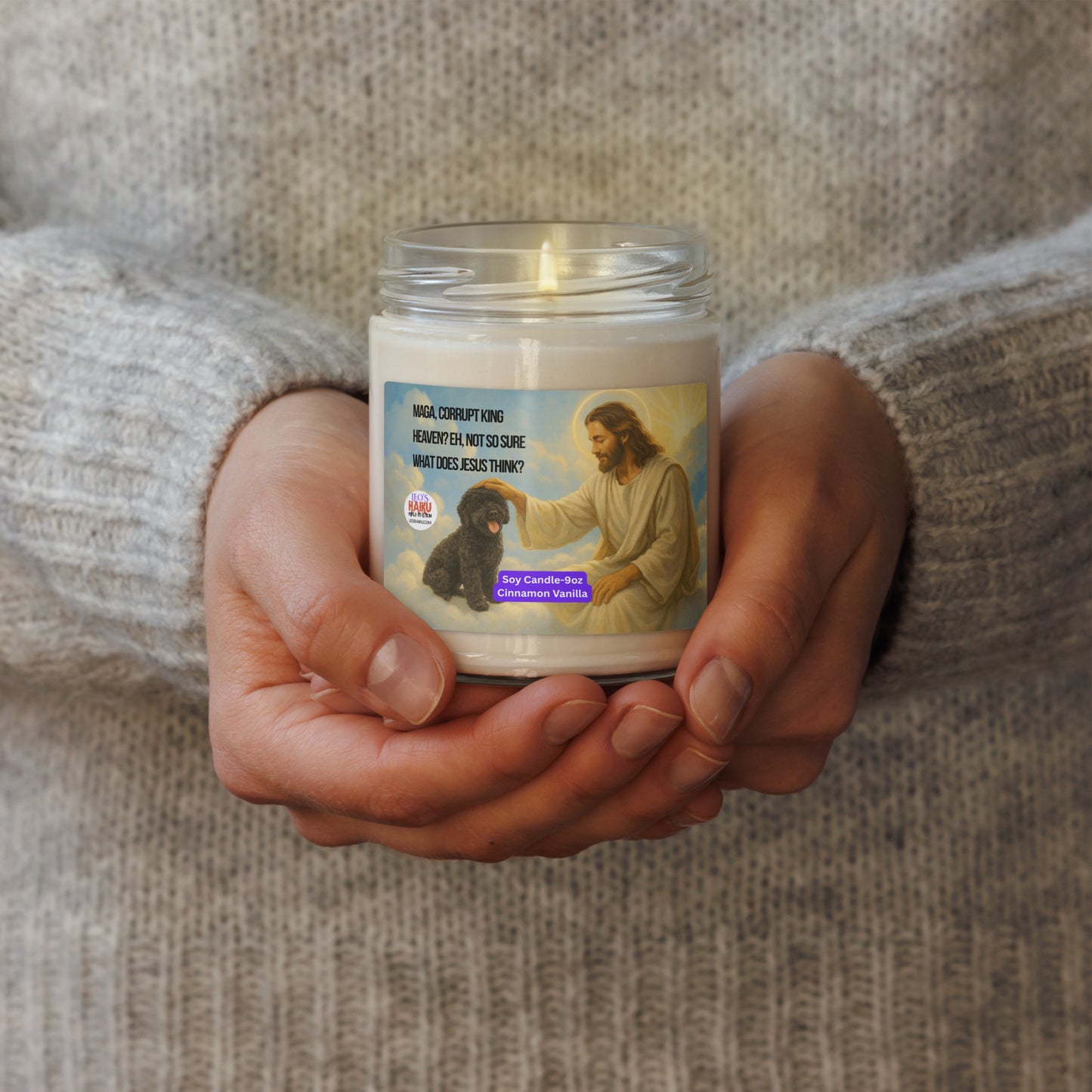 A person wearing a beige wool sweater is holding a lighted candle.  The label shows a small black dog and Jesus on a cloud as Jesus pats the dog's head.   Upper left is a political, satirical, anti-MAGA haiku that says:
MAGA, Corrupt King
Heaven? Eh Not So Sure
What Does Jesus Say.
The leoshaiku.com text logo is below that.  Bottom center is white text on a purple background that say:
Soy Candle - 9oz
Cinnamon Vanilla