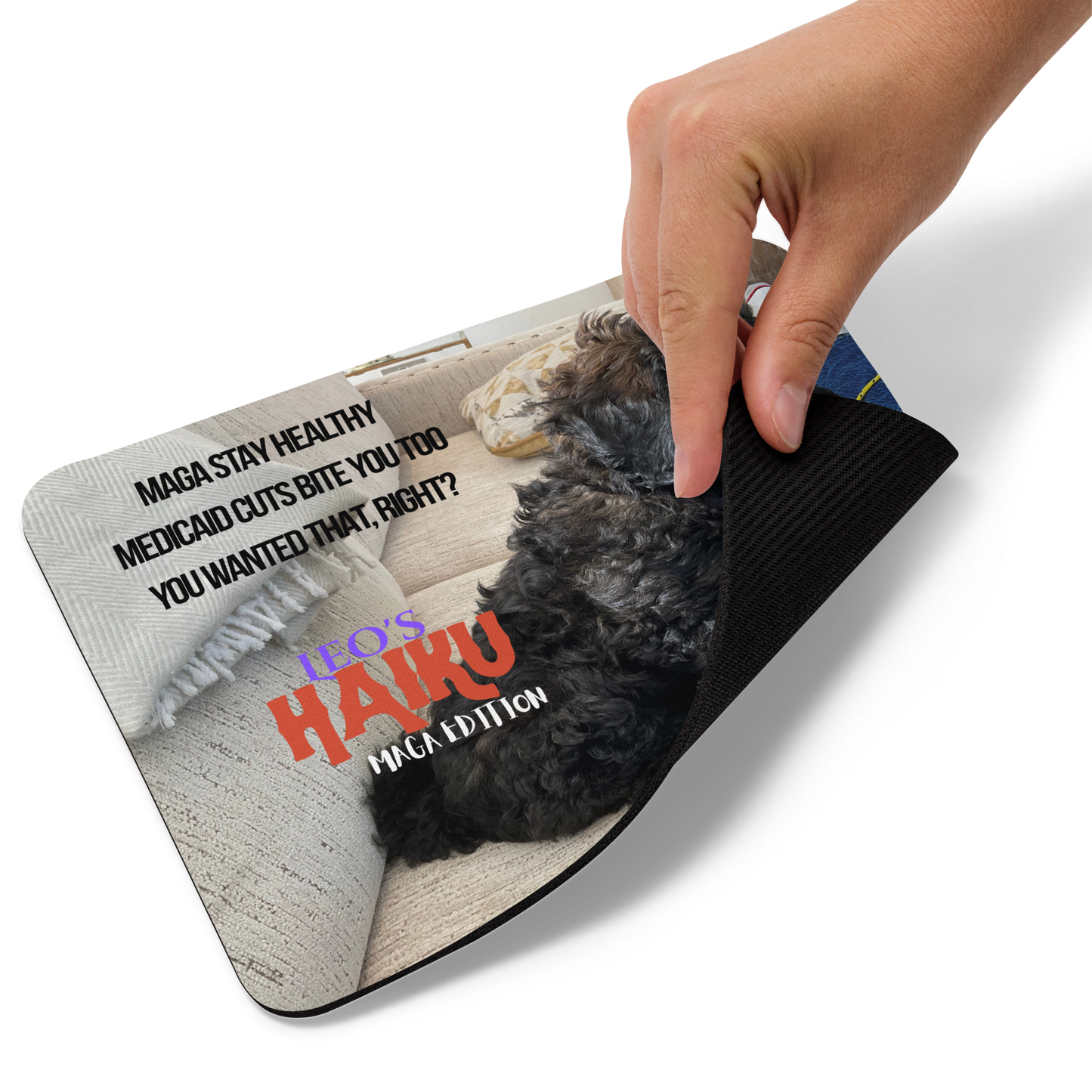 A hand lists the lower right corner of a standard-sized mouse pad printed with the side view of a poodle sitting on a beige couch, political satire in Haiku format, and branding elements.  This view shows the thickness of the pad.  