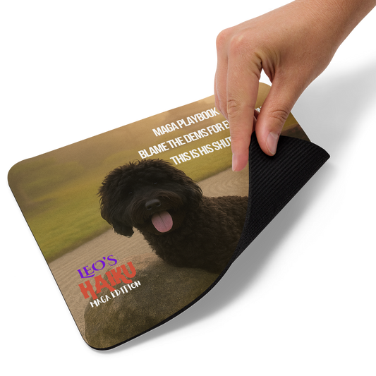 A hand lifts the bottom right corner of a standard-sized mouse pad printed with a Zen garden in golden light.  Poodle leans on rock beneath a Haiku of political satire.  This view shows the thickness of the pad.