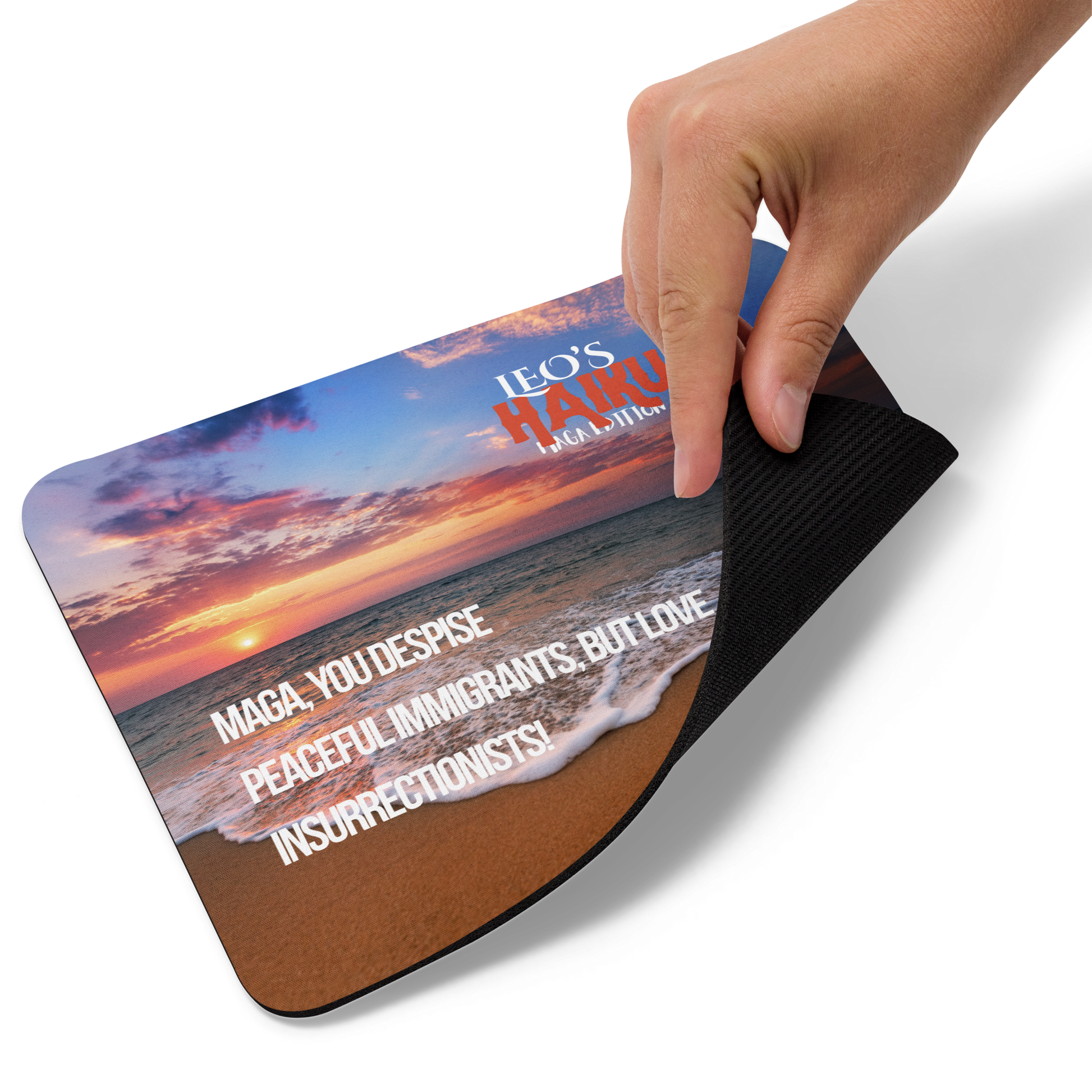 A hand lifts the bottom right corner of a standard-sized mouse pad printed with a sunset on the beach, a poodle, and political satire in Haiku format.  This view shows the thickness of the pad.