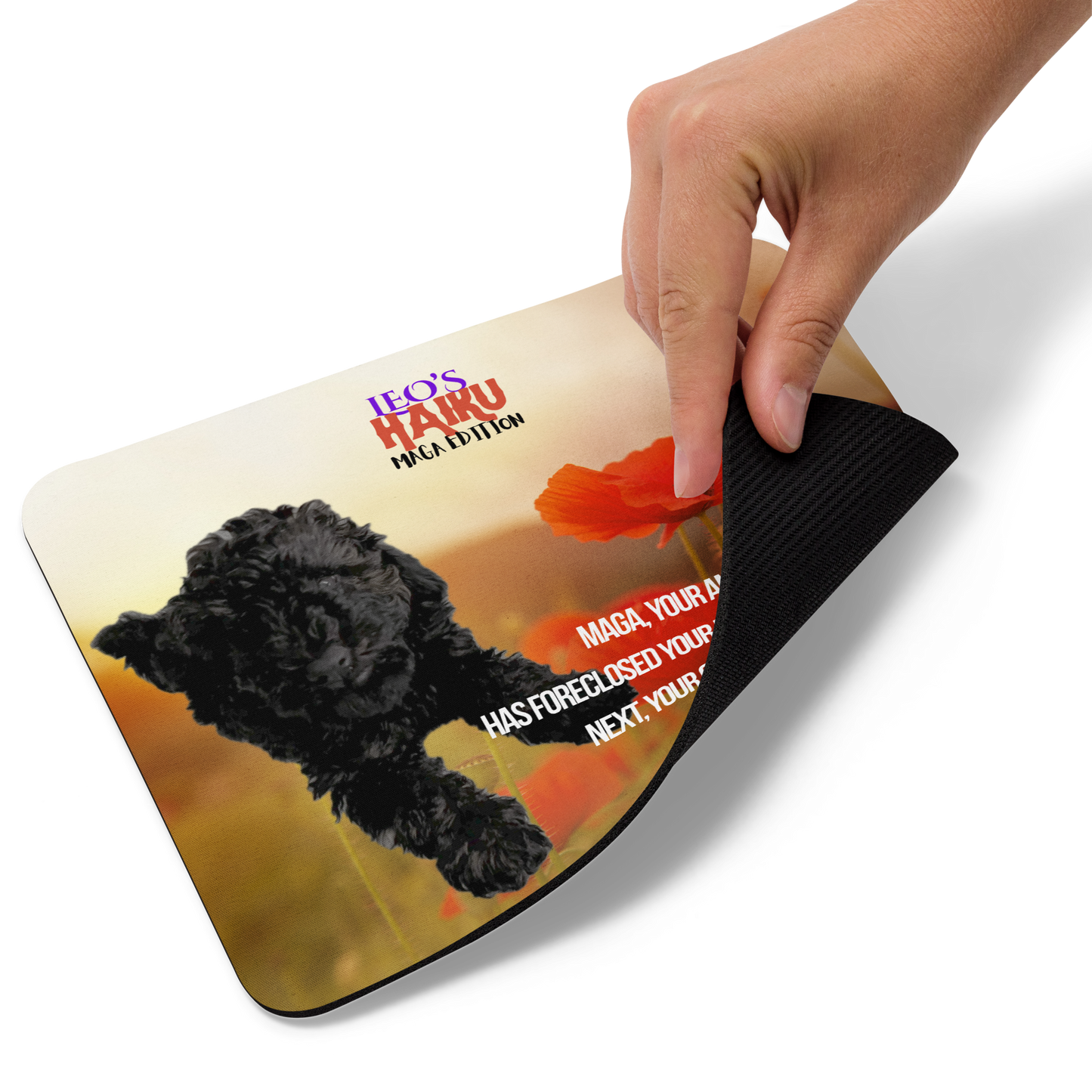 Hand lifts the bottom right corner of standard-sized mouse pad printed with a background of red poppies and other plants, a reclining dog, and political satire in Haiku format.