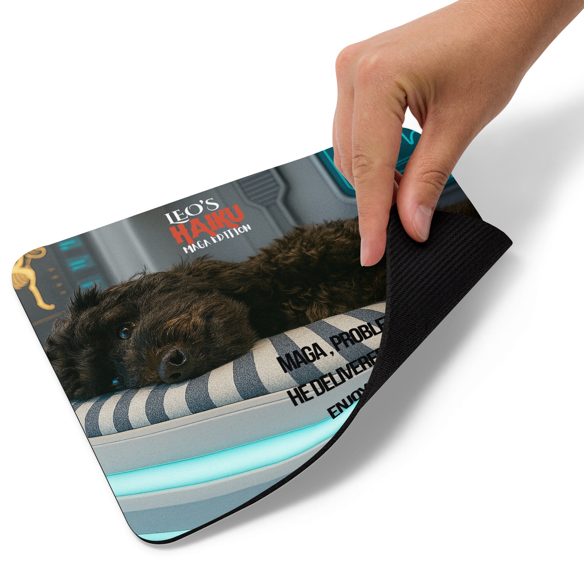A hand lifts the right lower edge of a standard mouse pad with image of black dog in high tech med bed; political satire text, and branding.  This view shows the thickness of the pad.